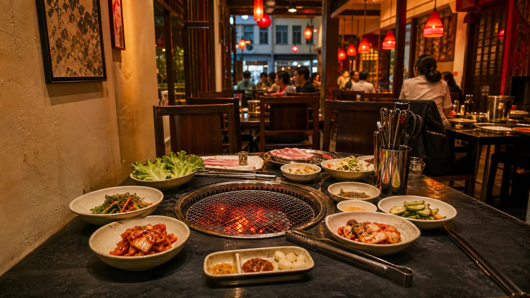 A prepared Korean barbecue table with glowing charcoal, banchan and the lively restaurant dining room beyond